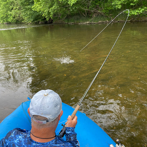 man fighting a fish from a blue raft on a river - the Shenandoah river of Virginia and the fish is a smallmouth bass 