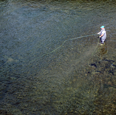 fly fishing person standing in the water fishing across the current with a fly rod and streamer or minnow imitation